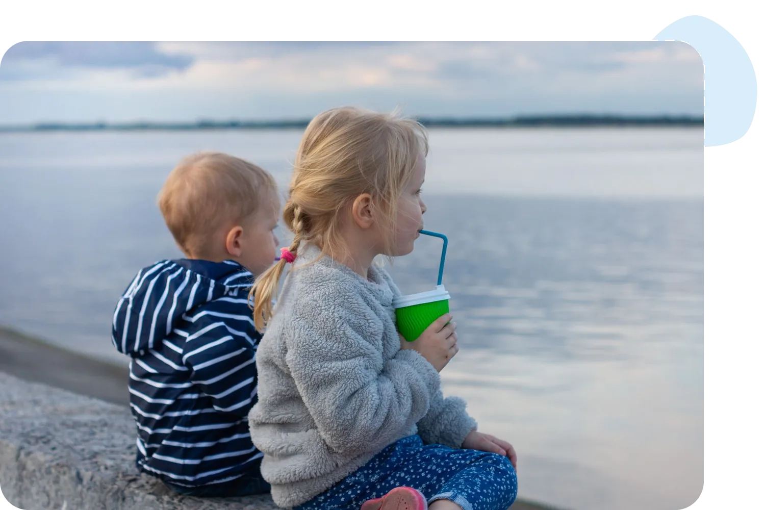Two small children drinking from cups with straws by the water